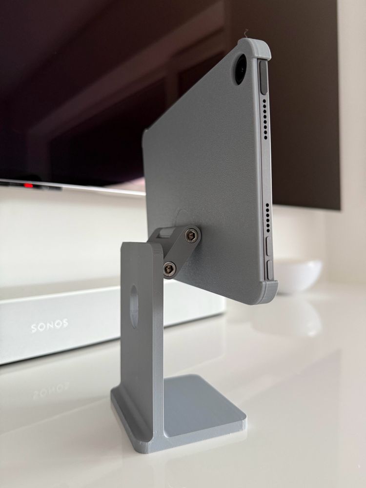 iPad mini in a grey 3D printed holder that looks like a Apple Studio Display stand. It’s standing on a white table. Shown from the back.

The stand shows a two-point hinge that enables the iPad to move in different angles.