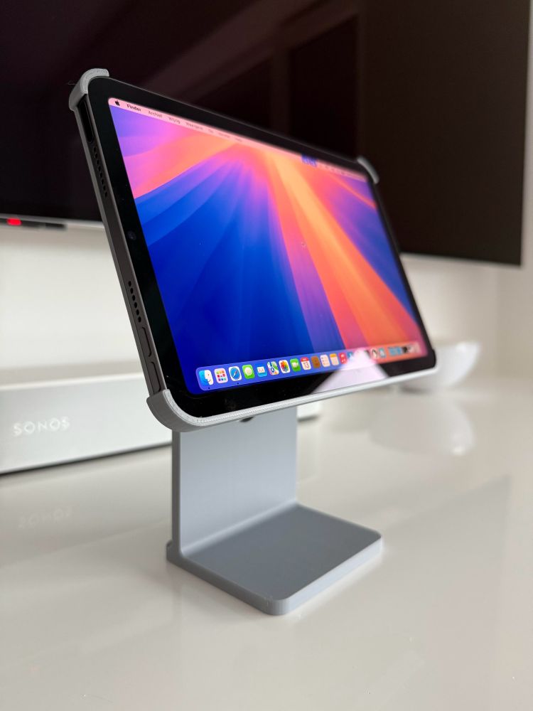 iPad mini in a grey 3D printed holder that looks like a Apple Studio Display stand. It’s standing on a white table. 