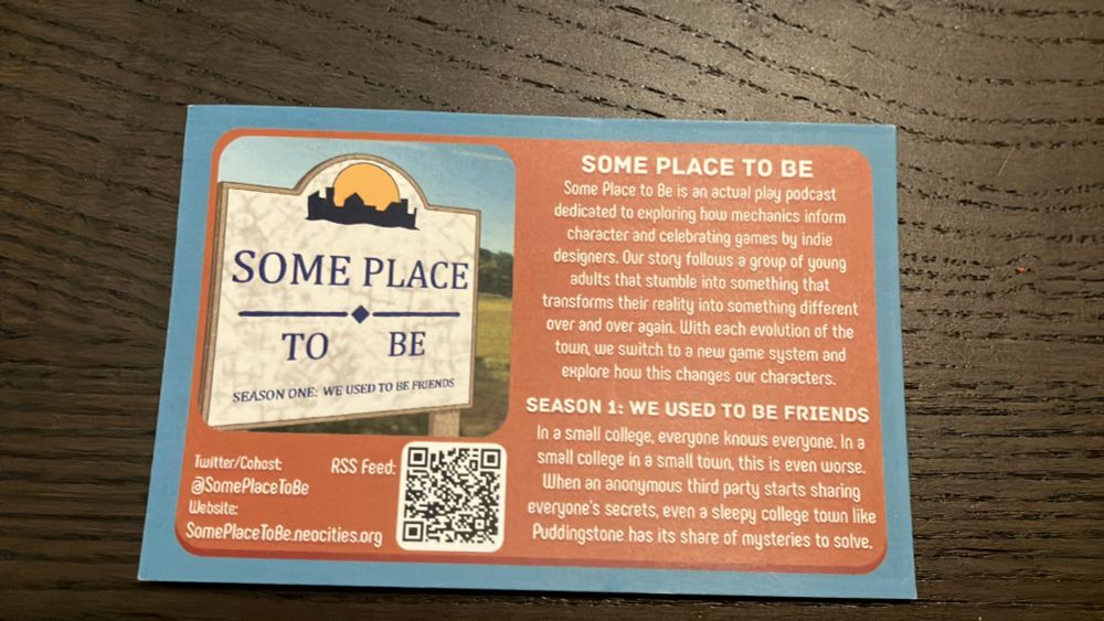 A photograph of a postcard with the season 1 album art, Twitter/cohost ats, website link, RSS QR code, and text that reads Some Place to Be is an actual play podcast dedicated to exploring how mechanics inform character and celebrating games by indie designers. Our story follows a group of young adults living in a small town full of mysteries to solve. They'll end up stumbling into something that transforms their reality into something different over and over again while only the main characters seem to notice. With each evolution of the town, we switch to a new game system and explore how this changes our characters. Season 1 We Used to Be Friends In a small college, everyone knows everyone. In a small college in a small town, this is even worse. When an anonymous third party starts sharing everyone's secrets, even a sleepy college town like Puddingstone has its share of mysteries to solve.