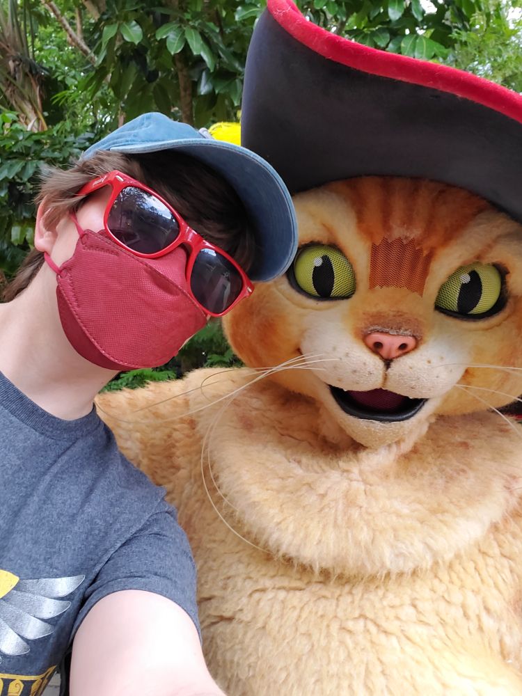 A selfie in a mask, sunglasses, and baseball hat with Puss in Boots