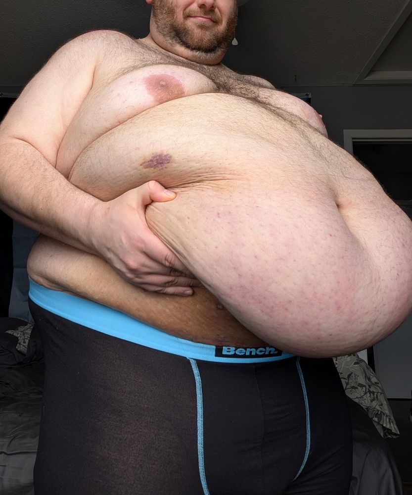 Angled front shot of a superchub. He's hefting up his belly, exposing a bit of his underwear waistline. It looks heavy! 