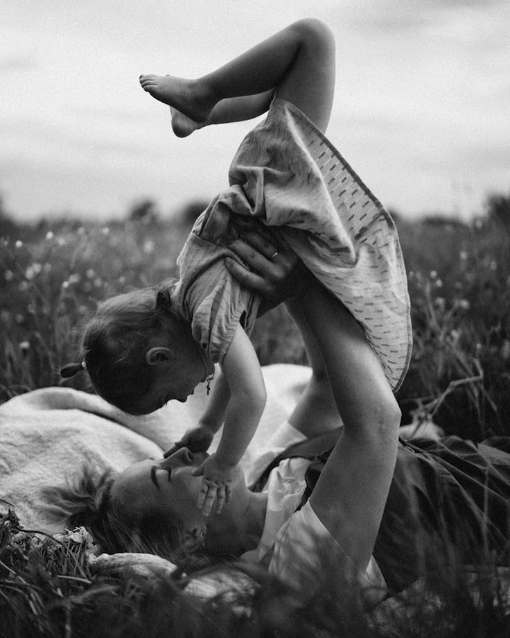 Mom laying in grass holding daughter & swinging her up in the air…