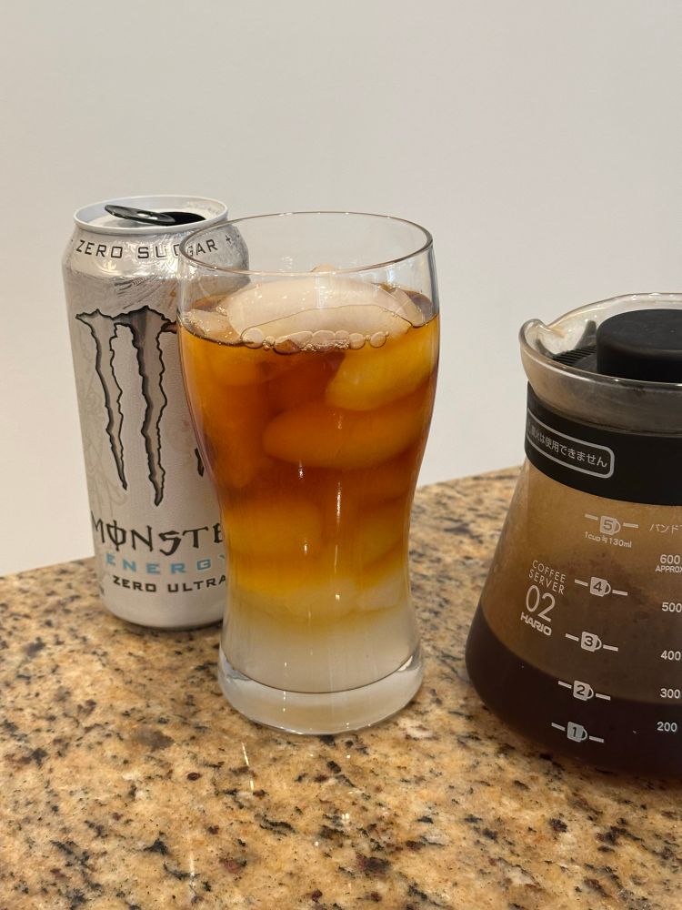 Photo of a glass filled with ice and with half pourover coffee mixed with Monster Zero Ultra, and the glass is flanked by the can of Monster Zero Ultra and a Hario coffee carafe