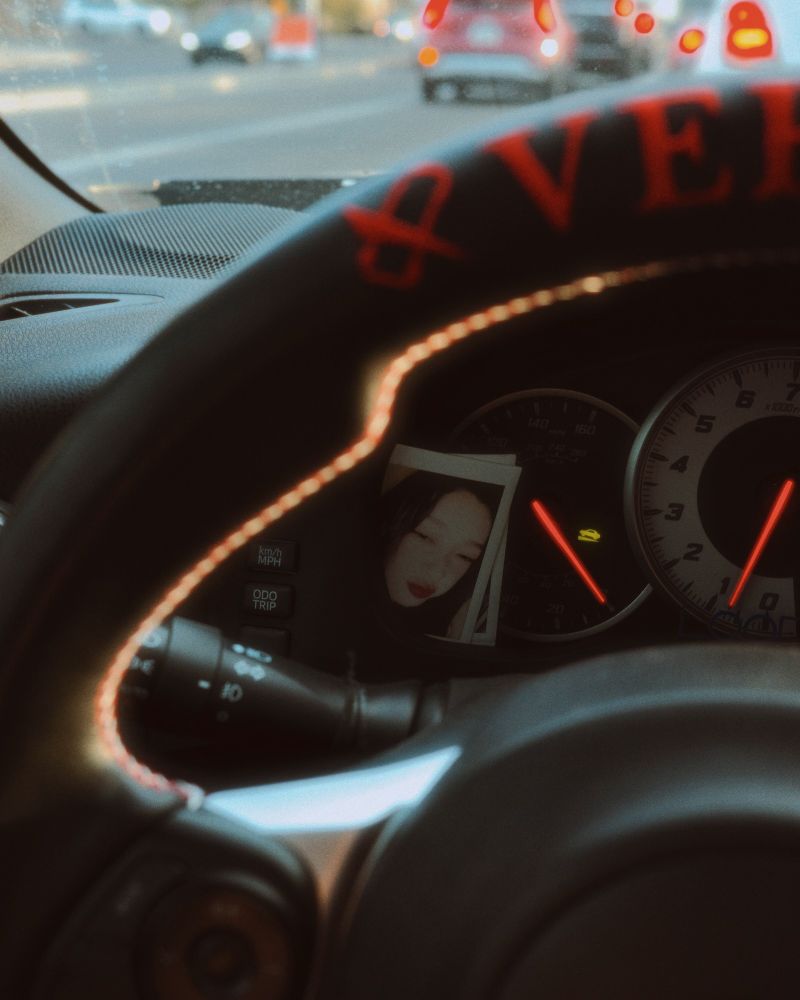 interior car shot from the driver's perspective, with its focus on a polaroid/instax by the speedometer