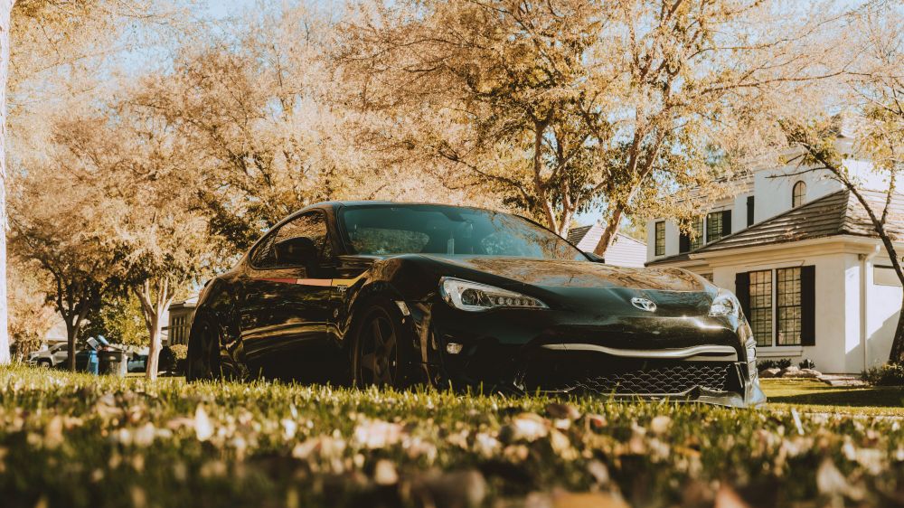 Toyota 86 TRD SE, slammed to the ground, with some grass to hide how low it is, and some yellow trees in the background.