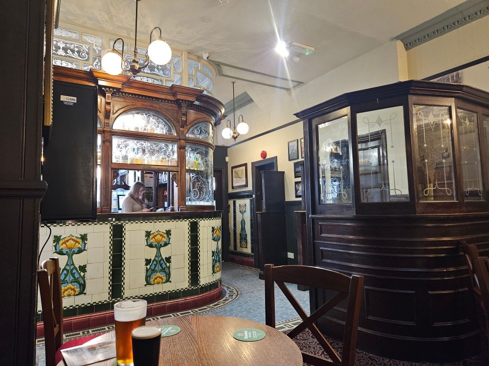 Art nouveau tiled pub interior. There are etched glass panels with a few serving hatches