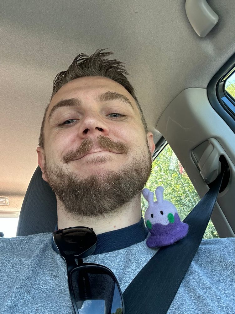 The author riding in the car with a felted Goomy on his shoulder.