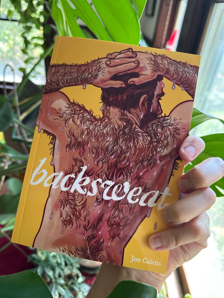 the author holding a copy of his new book, backsweat amidst the leaves of a monstera. The book's cover features a man's sweaty, hairy back.