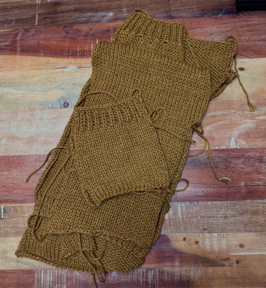 Pieces for a Campus Cardigan are stacked on a wood table. The yarn is Vintage Berroco Chunky in the color Chana Dal. 