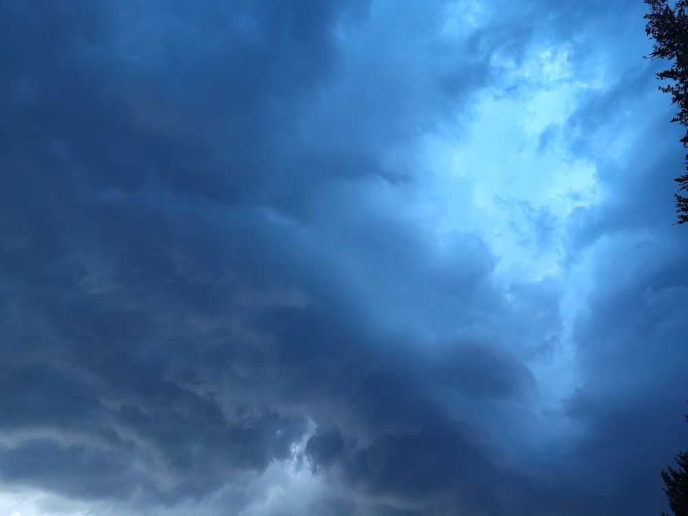A view of the underside of a developing thunderstorm, an opening on the edge of it led to a view of blue open sky that cast the rest of the storm in a deep blue hue. 
