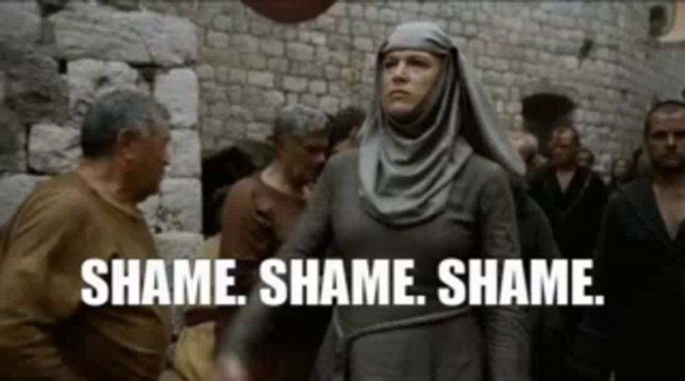 a woman in a hijab is standing in front of a crowd of people and saying `` shame shame shame . ''