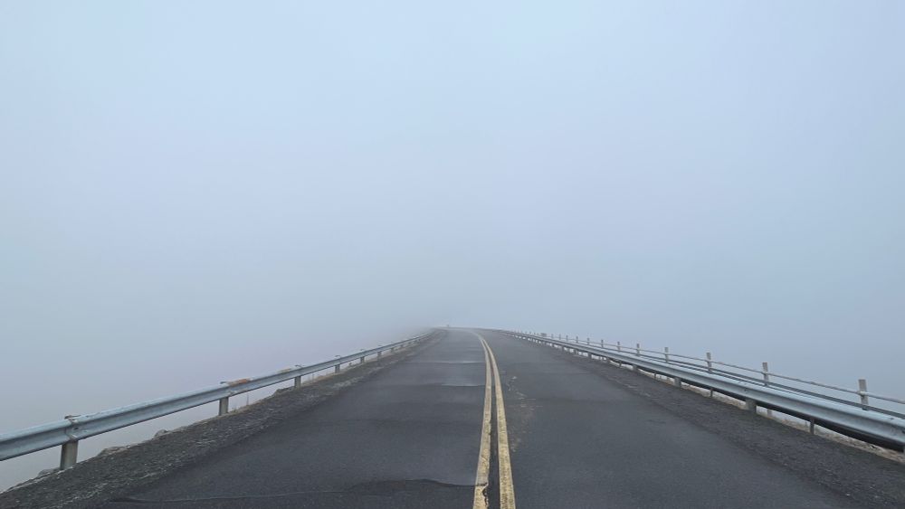 An empty road disappears into a cloud of fog