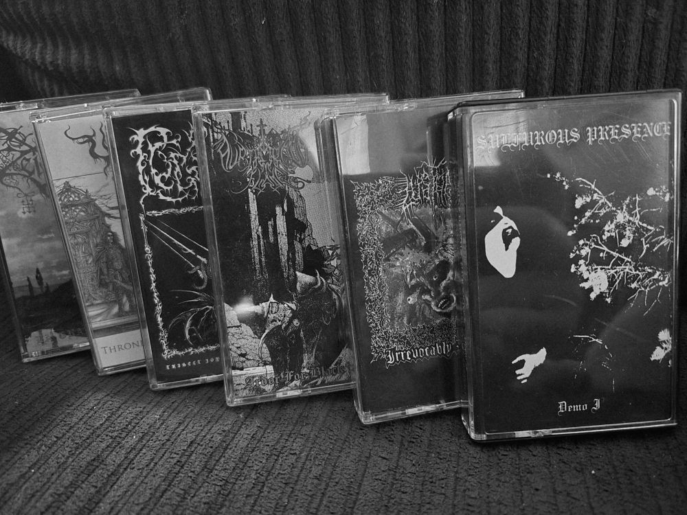 A row of black metal tapes featuring:

Zeicrydeus - La Grande Heresie
Valdrin - Throne of the Lunar Soul
Lucifixion - Trisect Joys of Pierced Hearts
Auriferous Flame - Ardor for Black Mastery
Lust Hag - Irrevocably Drubbed
Sulfurous Presence - Demo I