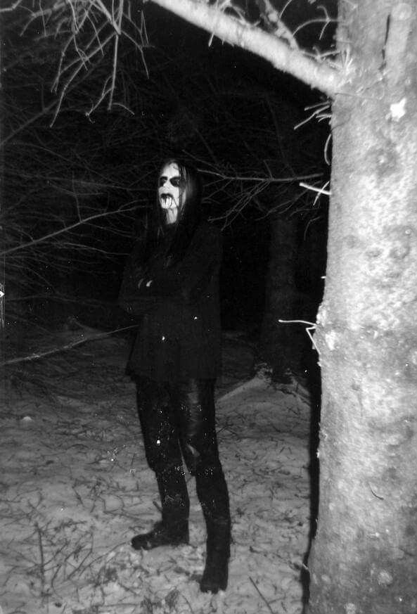 A guy dressed in black wearing corpsepaint standing alone in a snowy forest