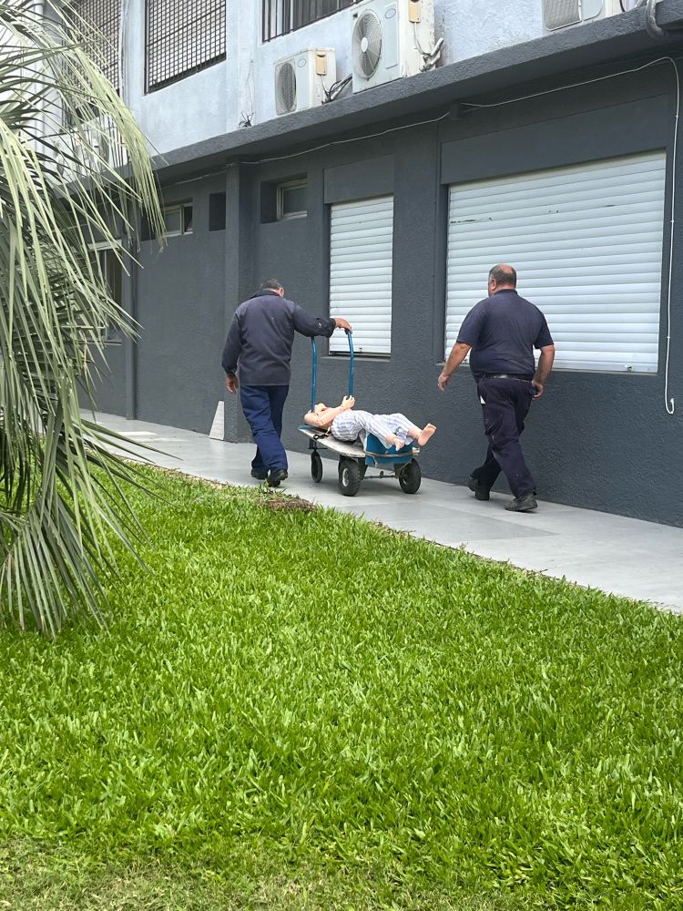 Two men wheel a mannequin away on a dolley. The mannequin is wearing striped pajama pants and looks vaguely like a dead body.