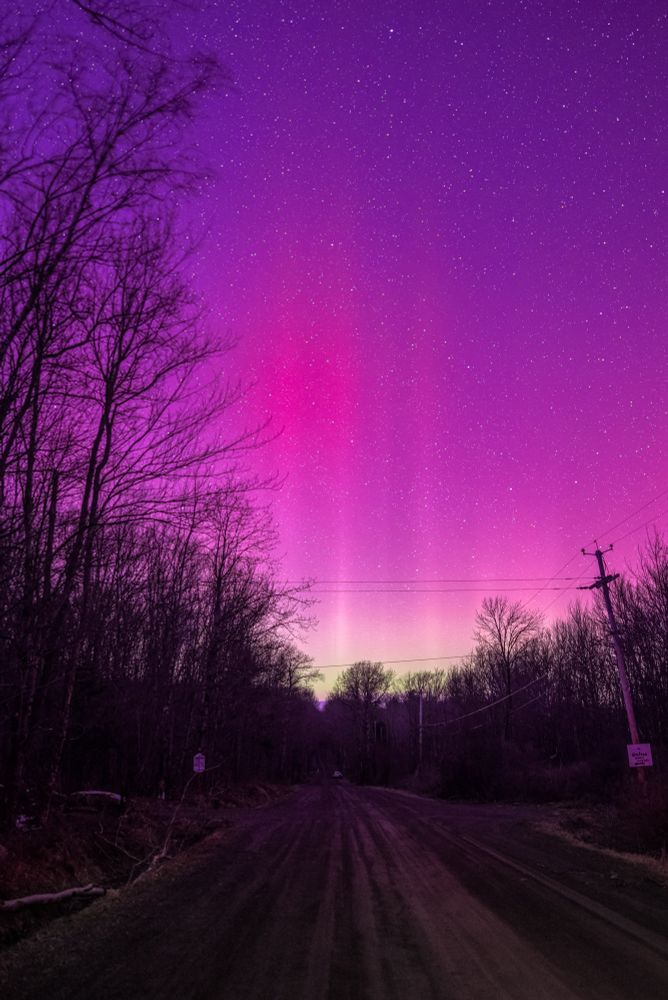 Pink, purple, and reddish hues of the northern lights in a starry night sky over a road. 