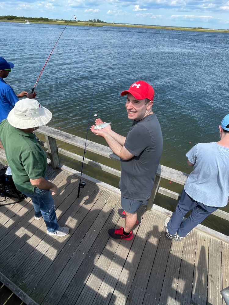 A person holding a small fish in their hands while standing on a fishing pier.
