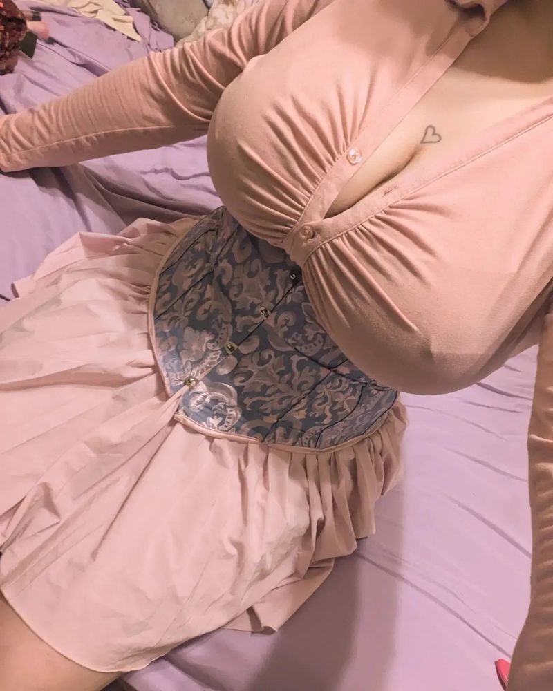 Lush sitting down with a pink long sleeve blouse, blue and pink corset, and a pink skirt. You can't see their head or face.