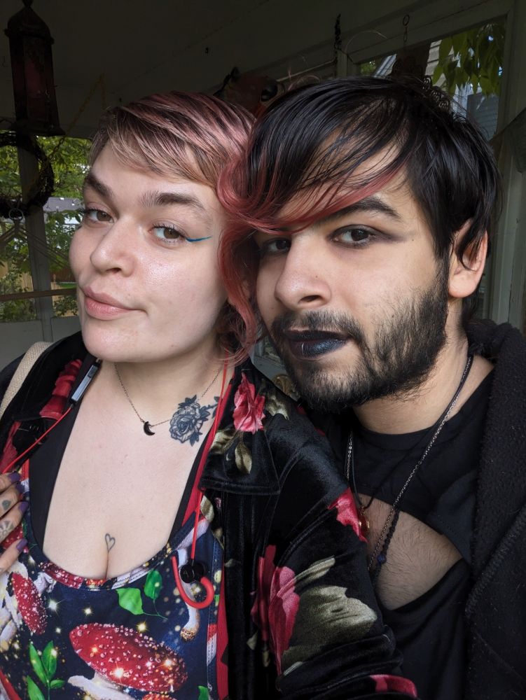 Lush wearing a mushroom patterned jumper with a velvety black cardigan red roses and Umbra with black lipstick wearing a black top and black sweatshirt