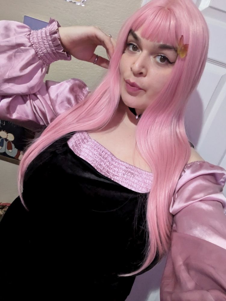 Lush wearing a black velvet sleeveless dress with light pink flowy sleeves underneath. Lush has light pink long hair with bangs and is wearing a black choker and a butterfly hair clip