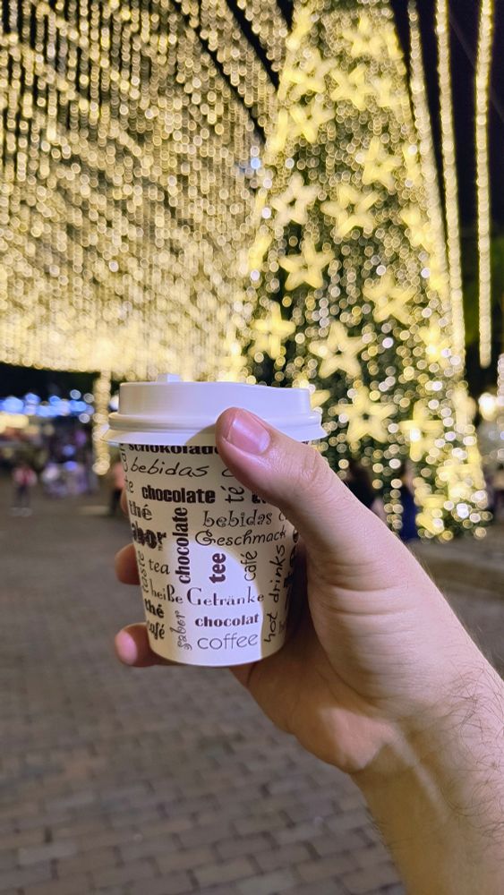 Coffee in a paper cup, in front of a giant ass Christmas tree with the Christmas lights on. 