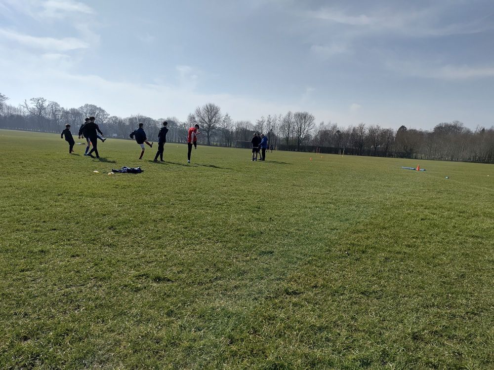 A group of young teens warming up for a football match on a grass field in the sunshine 