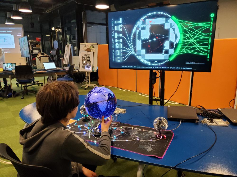 A teen boy, seeing from the back, sitting in front of the globe and looking at the screen. He's rotating the LED globe to play the game.
On the screen we can see the game with a black and white representation of the earth and some touches of green for life and red for asteroids.
