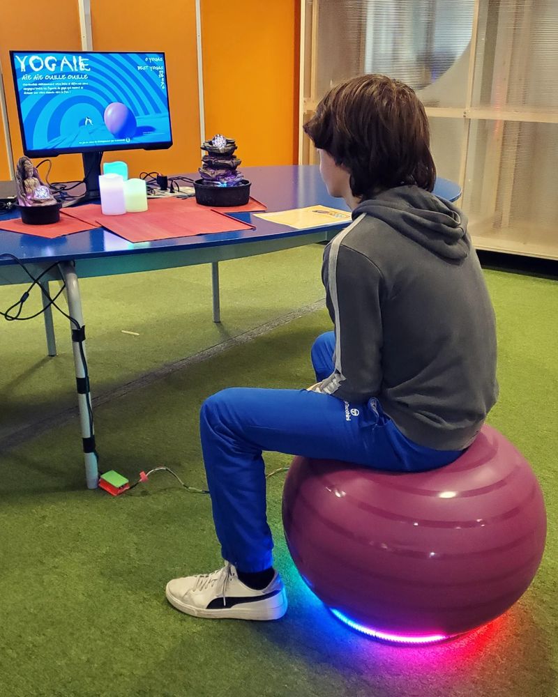 A kid is sitting on the yoga ball ready to jump to play the game on screen.