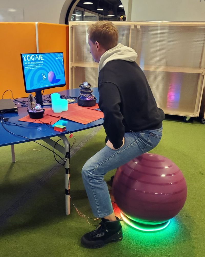 A guy is standing above the yoga ball ready to dit on it.