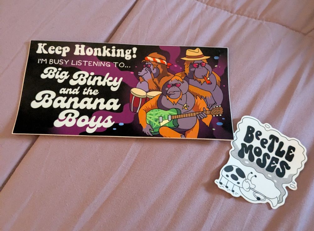 bumper sticker one is an image of three incredibly cool orangutans, white text on a purple and black swirl background that says: KEEP HONKING! I'M BUSY LISTENING TO BIG BINKY AND THE BANANA BOYS

sticker two is a black and white sticker of a ladybug blowing or smoking through a horn that says "Beetle Moses" on it