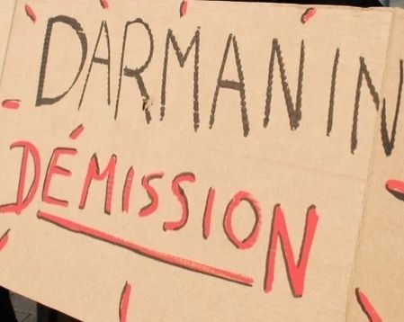 Image d'une pancarte avec écrit dessus Darmanin (couleur noire) Démission (lettres rouge)