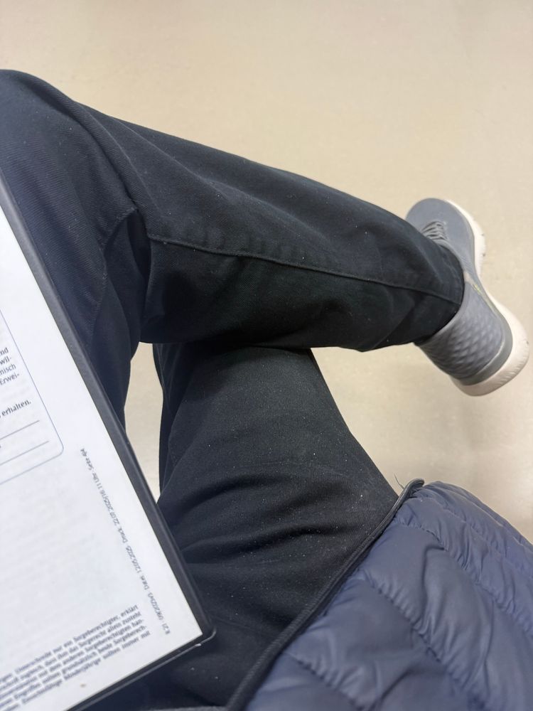 Wartebereichsfussboden, Beine übereinander gelegt, eine Ecke eines Aufklärungsblattes ist zu sehen. 