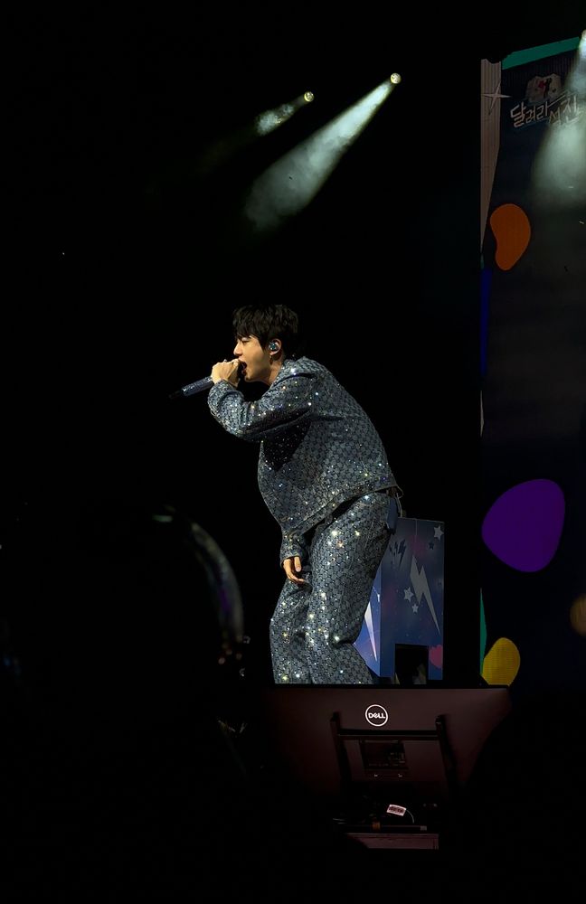 Jin standing on stage singing, still in his sparkly jeans, but this time he’s also got a matching sparkling denim jacket on. 