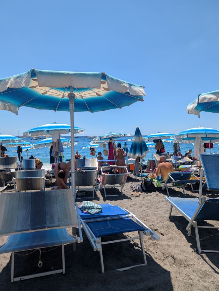 The Mediterranean in the distance with a beach and blue and white umbrellas and chairs. 