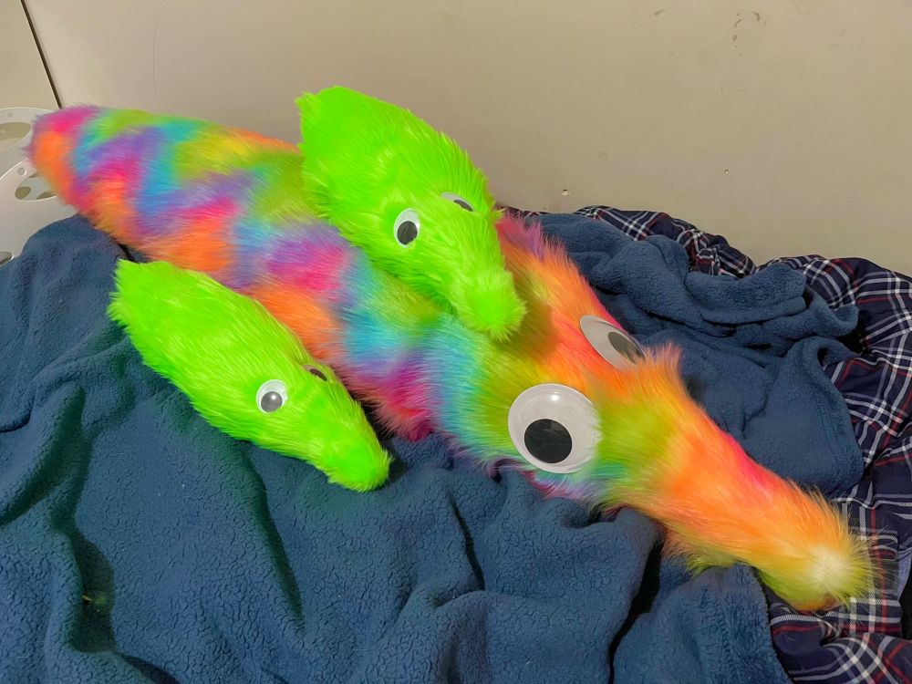 a giant rainbow worm on a string plush with two green radioactive babies
