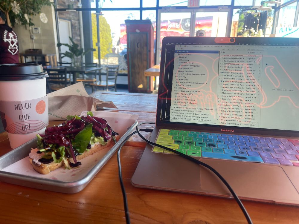 Photo of coffee cup with quote “never give up” and avacado toast to the left of a computer showing Zotero reference manager. In the reflection of the computer screen are the letters ABQ representing Albuquerque coffee shop. 