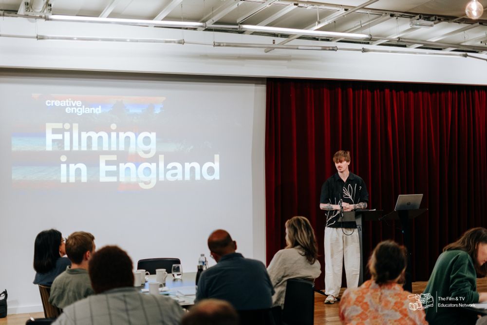 a man with brown hair presenting in front of a screen