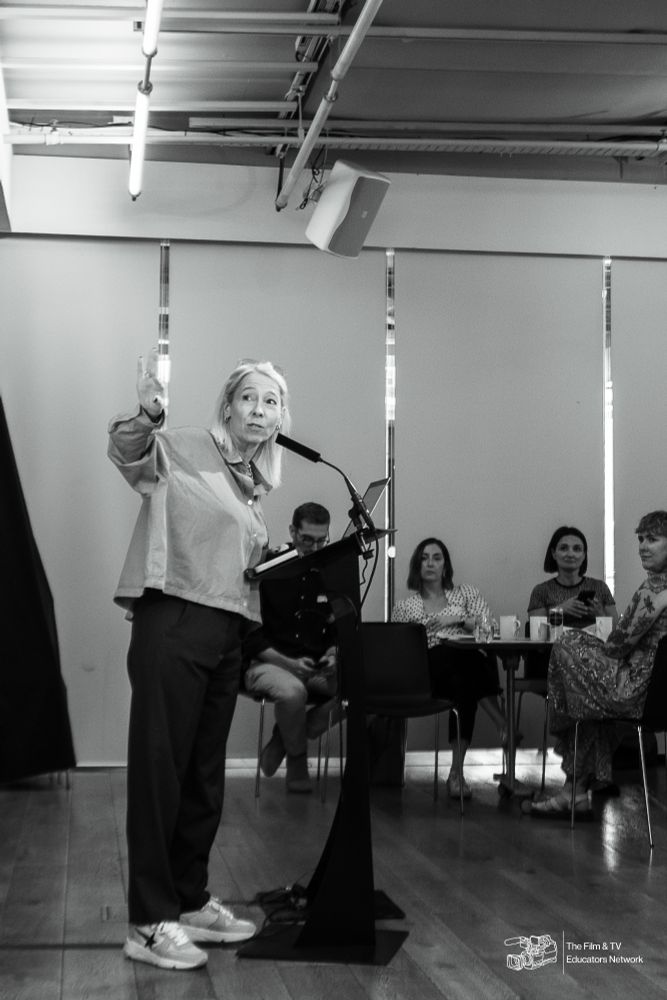 a woman with blonde hair presenting at a podium. the photo is in black and white. 