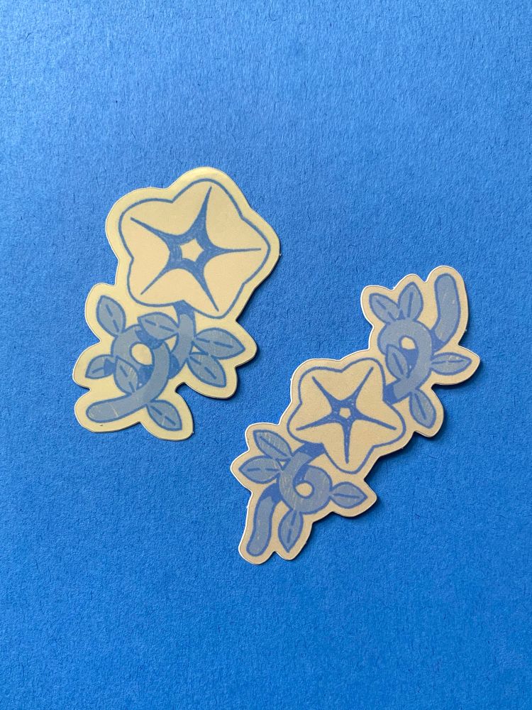 Two die-cut stickers against a blue background. Stickers feature beige flower designs with looping blue stems.