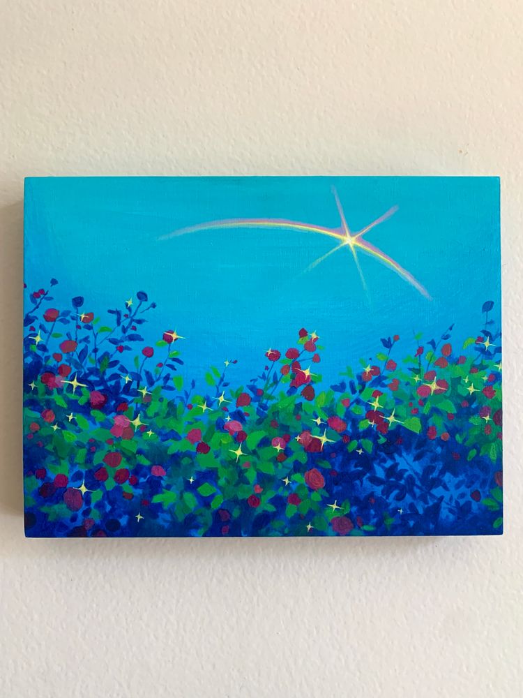 A photo of a rectangular painting against a white wall. Painting depicts a sparkling rosebush with blue shadows against a clear blue sky. A rainbow crosses the sky above with a star embedded in it.