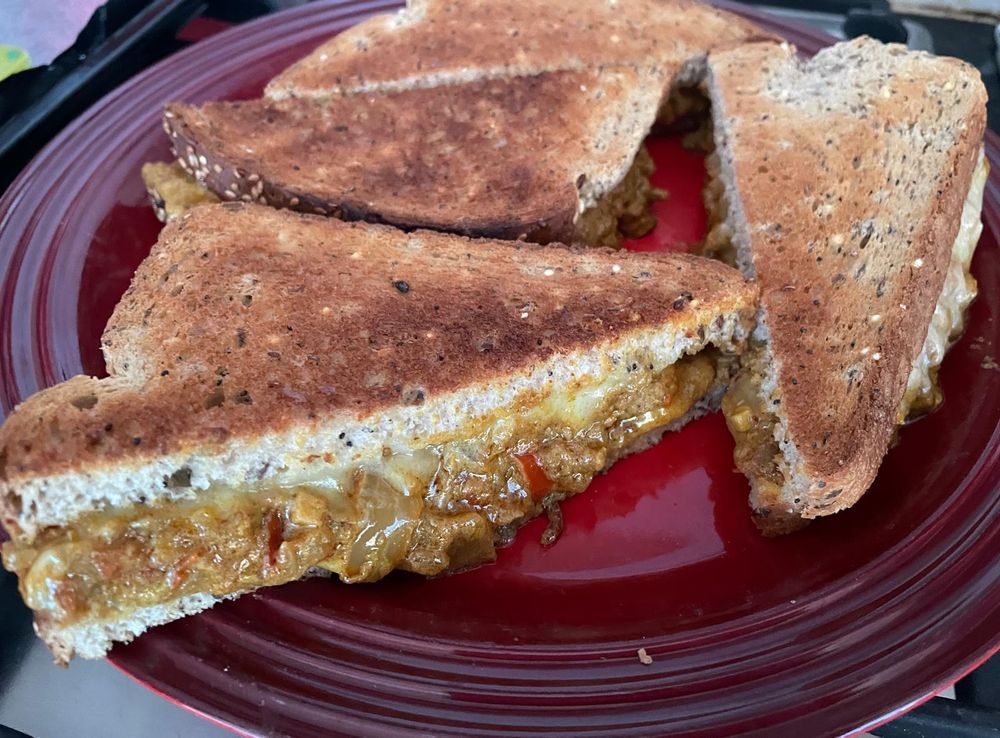 An image of four keema toasties on a red plate. Two slices of toasted bread with cheese and stuffed with Indian keema mince curry.