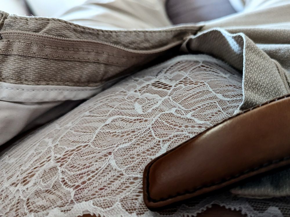 Foto von oben in die geöffnete Hose, man erkennt weiße Spitzenunterwäsche, die Scham ist flach