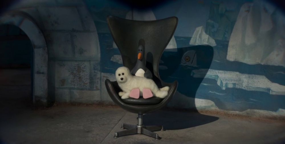 Scene from Vengeance Most Fowl with Feathers McGraw playing homage to Blofeld from the James Bond films. The villain penguin Feathers McGraw is sat in a black swivel chair with large, winged back. On his lap is a white sea lion which Fethers is stroking.