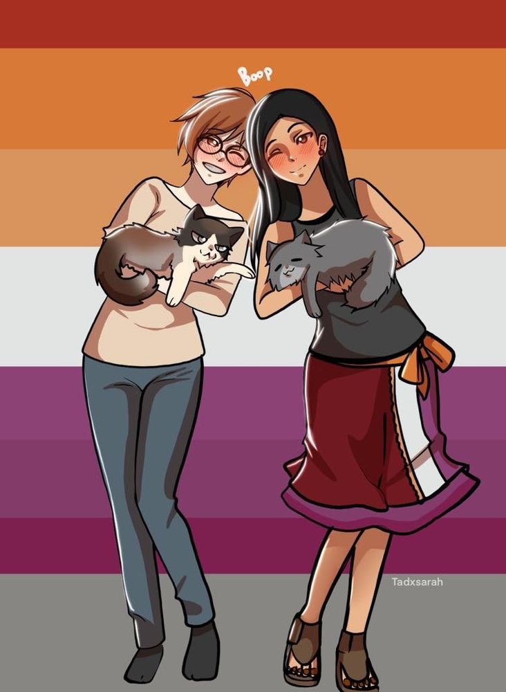 A redhead woman in glasses standing beside a brunette woman. They are both holding cats. 