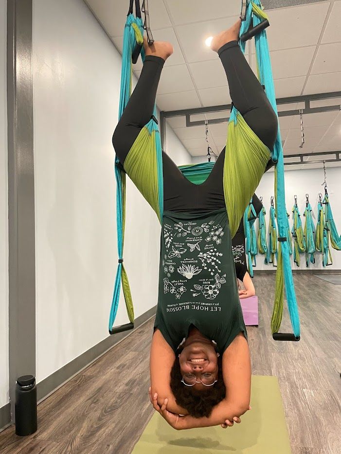saf hangs upside down in a trapeze yoga studio, with a smile on her face