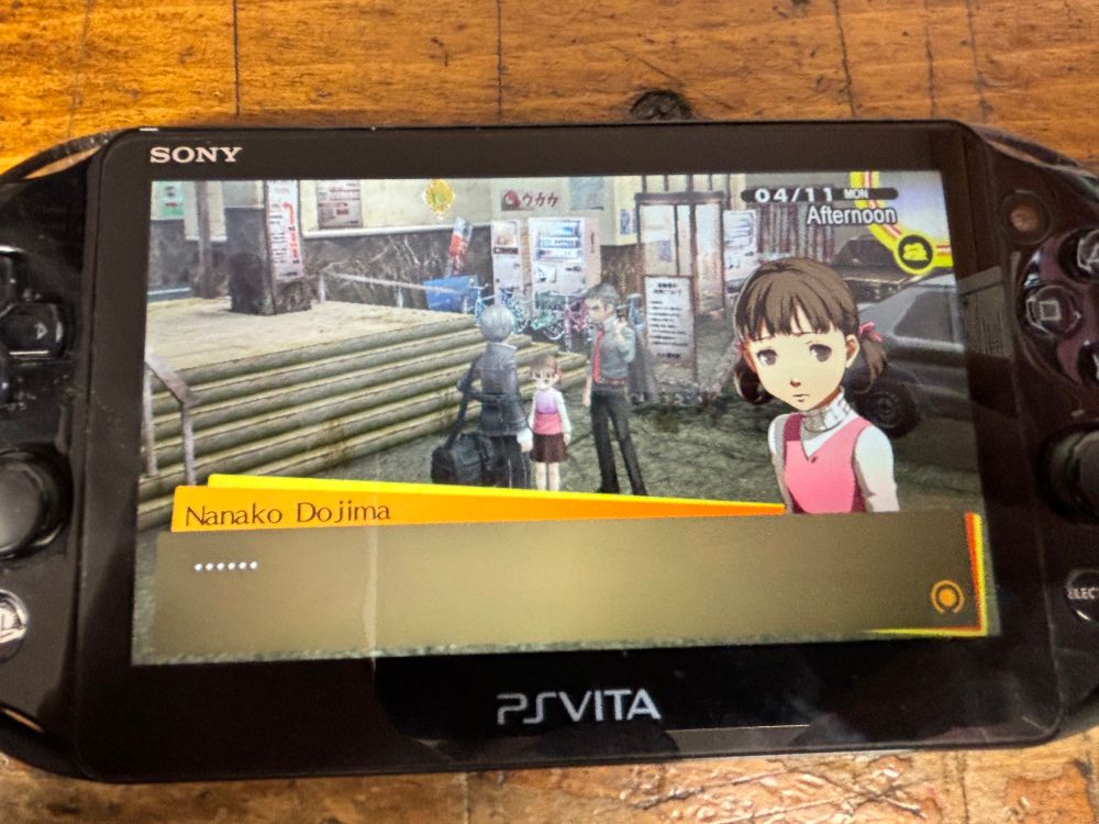 “Persona 4 Golden” played on a black PS Vita (Model 2000). Nanako, a child with kind of bad hair in a pink vest and white turtleneck, is on screen, with her text box a string of ellipses. The in-game date, 4/11, is displayed in the upper right corner. 