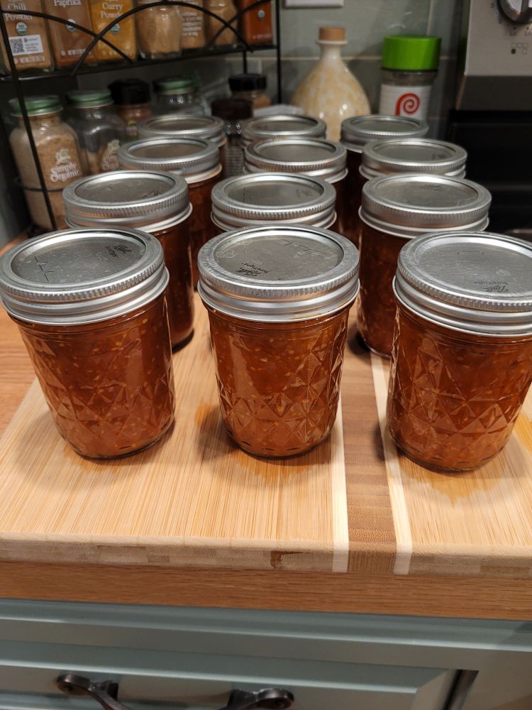 Twelve 8oz jars of homemade tomato-based pizza sauce cooling on a wooden cutting board 