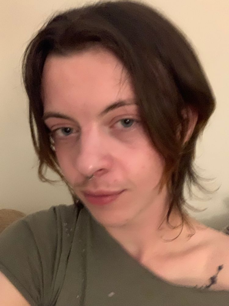 selfie of me with a wide necked light green shirt on, looking sleepy. my hair is soft, smooth, dark brown, and kind of chin/neck length, and also did i mention soft.