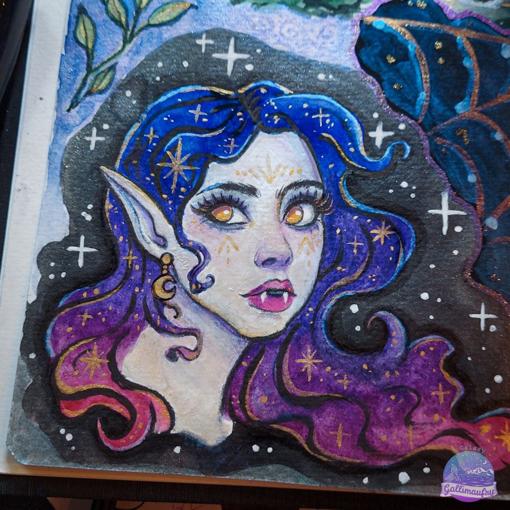 Close up on one of the paintings in the sketchbook, a space vampire. She has gold eyes and wavy hair in a blue/purple/pink gradient. She also has gold stars in her hair and a gold moon earring. Everything that is gold is shimmery metallic paint.