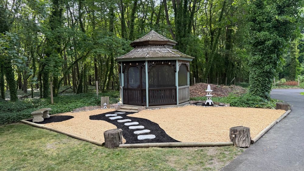 Gazebo painted in the colors of a Japanese tea house, set in a large area of stone pebbles, with a dark path with 8 stepping stones leading to entrance. 